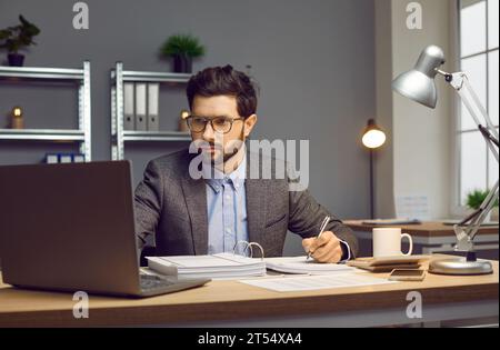 Focused businessman working on laptop and making notes on paper at workplace Stock Photo