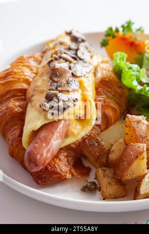 Brioche croissant egg and sausage sandwich with fresh fruits and vegetables at a cafe. Stock Photo