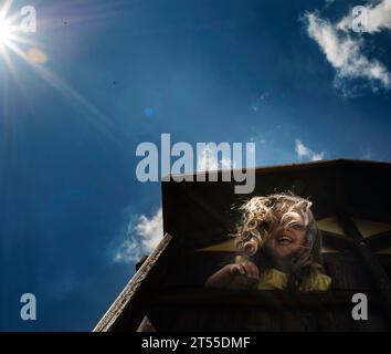 Happy little girl peeking over play house in summer Stock Photo