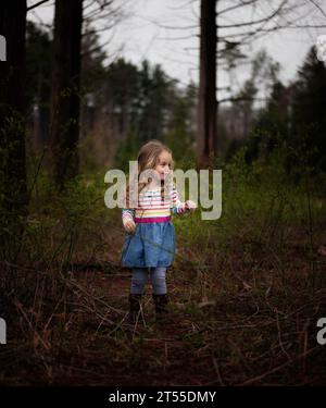 Beautiful little girl with blonde curls standing in pine forest Stock Photo