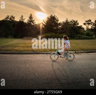 Young girl riding bike outdoors at sunset Stock Photo