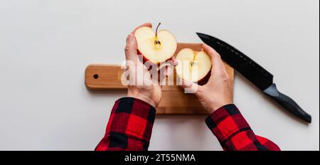 Two halves of an apple in male hands high angle view. Man cuts apple using knife. Stock Photo