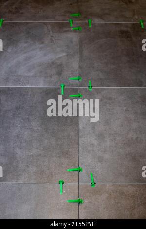 Tile levelling system, four plastic green clips with wedges. Close-up view, selective focus, blurred background. Stock Photo