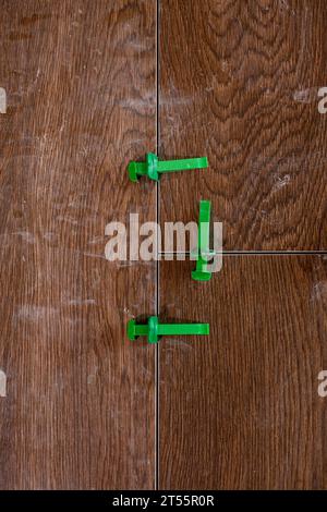 Tile levelling system, four plastic green clips with wedges. Close-up view, selective focus, blurred background. Stock Photo