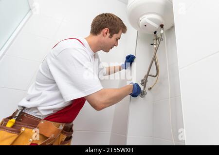 Closeup of plumber using screwdriver while fixing boiler or water heater, working on heating system in apartment Stock Photo