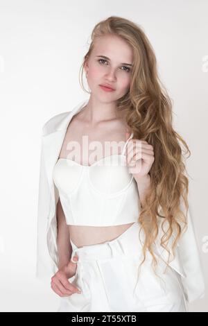 Portrait of fashion model looking at camera holding straps of cupped corset top with fingers of one hand, belt loop on trousers with other hand Stock Photo