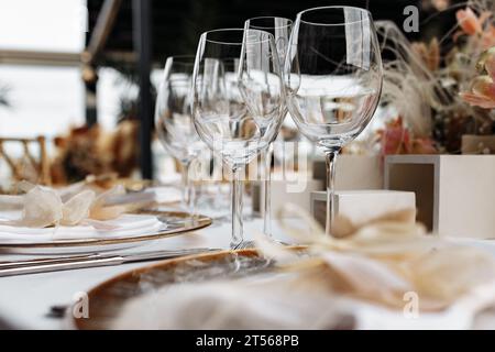 Transparent wine glasses on white tablecloth with plates and cutlery. Luxury restaurant close up view. Stock Photo