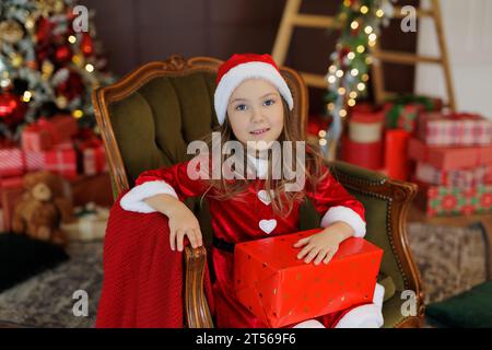 Little girl in red santa dress with present sitting on green armchair Stock Photo