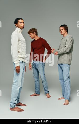 appealing young men in casual attire standing still and posing on gray backdrop, fashion concept Stock Photo