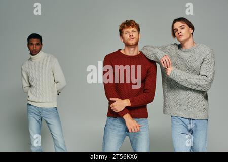 two young men in sweaters posing with their african american friend on backdrop, fashion concept Stock Photo
