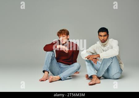 multicultural handsome male models in warm sweaters sitting on floor looking at camera, men power Stock Photo