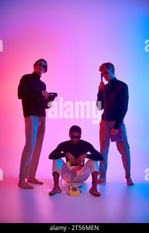 vertical shot of young multicultural men posing with landline phones surrounded by neon lights Stock Photo
