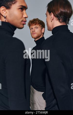 focus on young man standing near blurred interracial friends on gray background, fashion, vertical Stock Photo