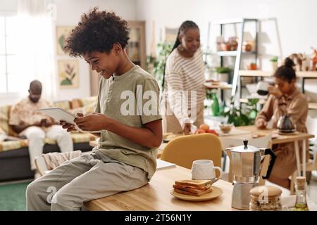 Smiling Black boy sitting on kitchen counter and watching animated cartoon on tablet computer Stock Photo