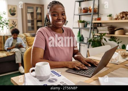 Portrait of happy Black woman working on laptop at home and drinking coffee Stock Photo