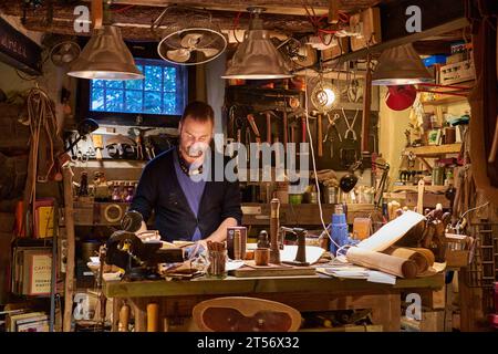 Alexis Fasoli, leather worker, stands in his shop in El Born, Barcelona, surrounded by tools and products for sale Stock Photo