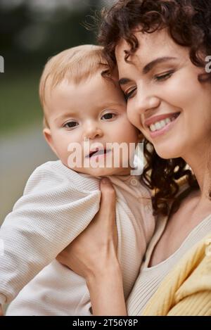 portrait of smiling woman with closed eyes embracing toddler child outdoors, happy moments Stock Photo