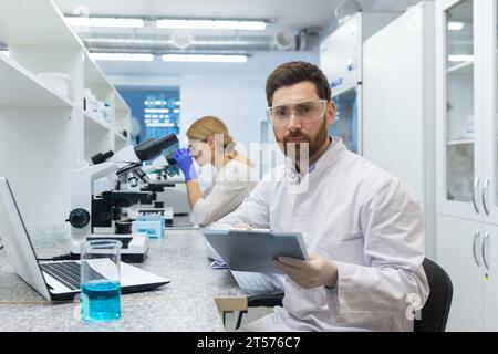 Portrait of serious concentrated thinking scientist, man looking at camera, using laptop at work and recording data, experienced scientist researcher. Stock Photo