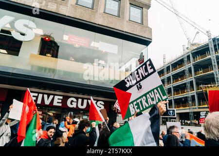 Protester holds up sign reading 'Silence is betrayal' written on Palestine flag in front of Five Guys. Newcastle Upon Tyne, England, UK - Oct 28 2023. Stock Photo