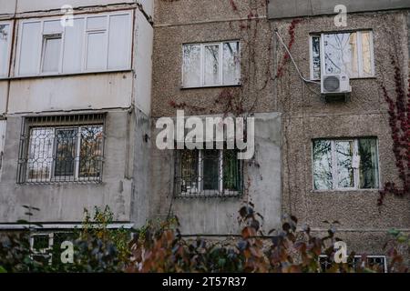 Different types Balconies and windows entwined with red ivy leaves in an old panel house. Facade Soviet apartment building. External air conditioner Stock Photo