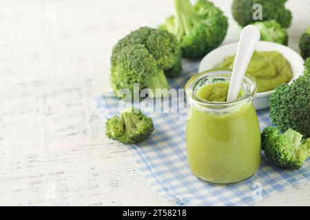 Green broccoli baby food in white bowl and jar on table. Green baby food. Child first feeding concept. Baby Natural Food. Production and menu of baby Stock Photo