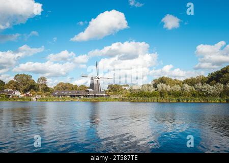 Historic wooden windmill on the banks of a river near Haarlem, in the west of the Netherlands. Dutch scenery on a sunny day. Stock Photo