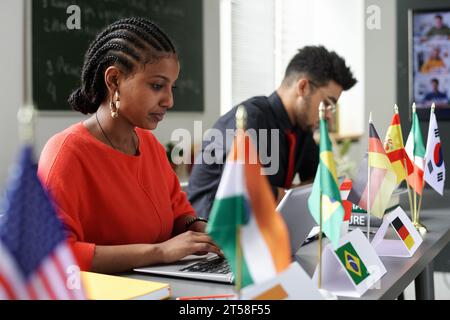 Group of international students sitting at table with flags and using gadgets at lesson in the classroom Stock Photo