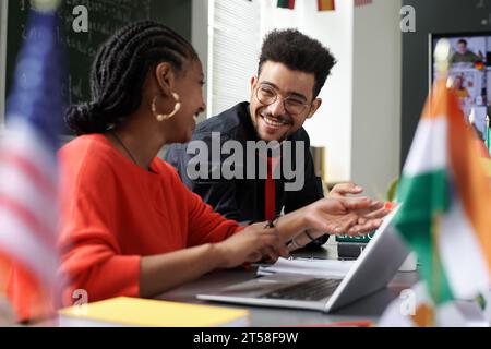 Multiethnic students discussing online work together while sitting at table with laptop Stock Photo