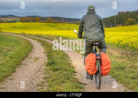 By bike through the colorful autumn. A cyclist in rain overalls rides along a picturesque dirt road in autumn. Stock Photo