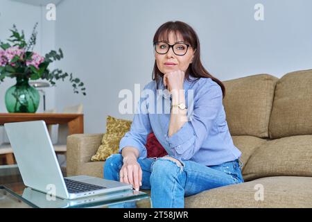Portrait of middle-aged woman with laptop on sofa in living room Stock Photo