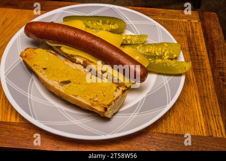 A sandwich with a French baguette and dijon mustard , Norwegian Jarlsberg cheese, Polish hotdog, and American Dill pickle on the side. Stock Photo