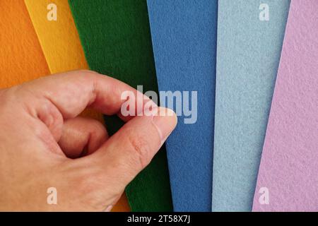 A man taking a blue sheet of felt out of a group of other colorful felt sheets. Close up. Stock Photo