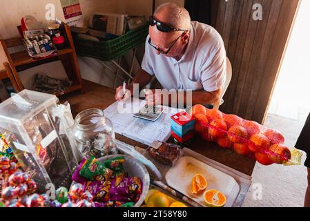 A shop owner does his daily accounts with a pen, calculator and book at a small shop in the Western Cape in South Africa Stock Photo
