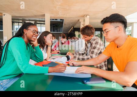 Happy multiracial group of high school students working together, sitting at library with notebooks, writing and using a laptop to search information. Young teenagers studying exams at university. High quality photo Stock Photo