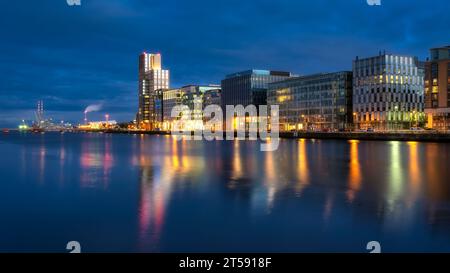 Modern offices and apartment buildings on Sir John Rogerson Quay and Poolbeg Powerstation chimneys, blurred Liffey River at dusk, Dublin, Ireland Stock Photo