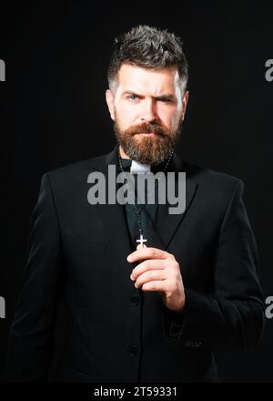 Religion concept. Handsome hispanic catholic priest man over black isolated background. Pastor or preacher praying, priest portrait of male pastor. Stock Photo