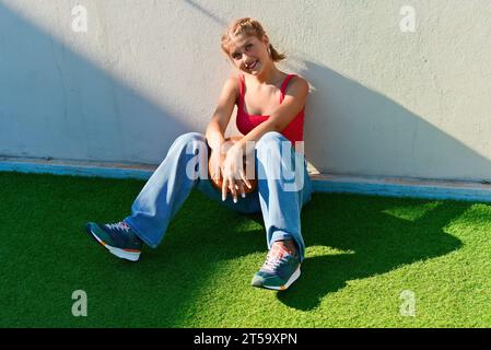 Cheerful teenage girl sitting on the sports ground. Stock Photo