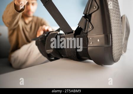 Close-up of an injured man putting on an ankle brace while sitting on a sofa Stock Photo