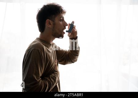 Indian guy suffering from asthma, Young man having asthma using the asthma inhaler for being healthy Stock Photo