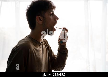Asthmatic man using an asthma inhaler during asthma attacks standing on window background Stock Photo