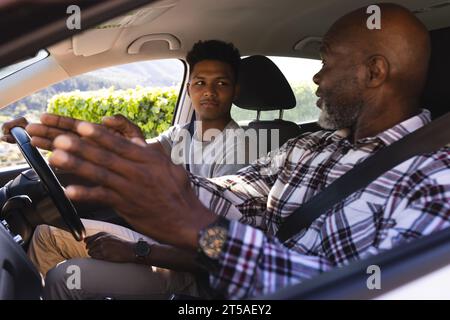 Happy african american father teaching and adult son in car during driving lesson. Transport, safety, car, driving lesson, learning, fatherhood, famil Stock Photo