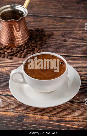 Double Turkish coffee in a white porcelain cup with a decorative coffee pot on a wooden table Stock Photo