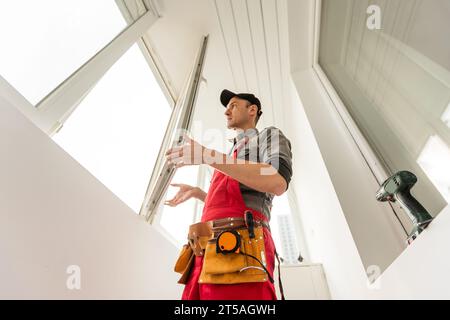 The installer worker in safe medical mask and overalls fixes a detail of the stiffener element with screws using an electric screwdriver to the wall Stock Photo