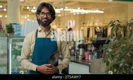 Indian male coffee store worker Arabian waiter Muslim man startup owner Hispanic small business employee guy in apron posing at cafe restaurant Stock Photo