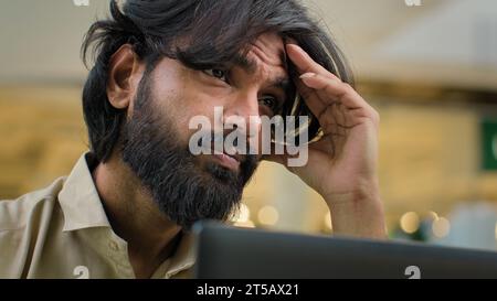 Exhausted Indian bearded businessman taking off glasses feel headache eye strain discomfort. Overworked Arabian man worker feeling fatigue after Stock Photo