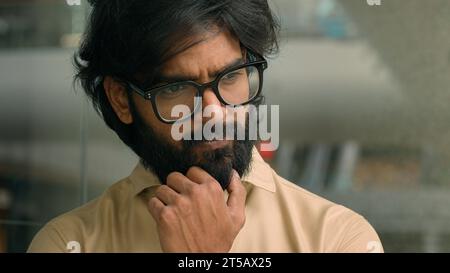 Thoughtful worried Arabian businessman thinking of future business challenges financial crisis. Doubtful serious pensive Indian bearded man in glasses Stock Photo