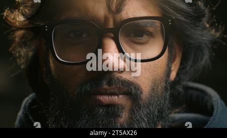 Extreme close up serious calm Arabian male face in eyeglasses looking at camera portrait headshot Muslim guy bearded Indian man look eyesight vision Stock Photo