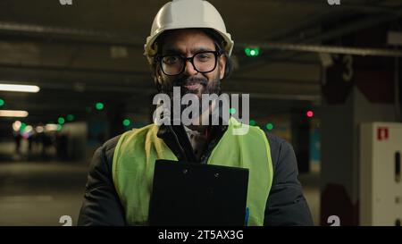 Indian contractor mechanic guy in helmet and glasses smile posing with clipboard folder. Arabian bearded man in eyeglasses worker male specialist Stock Photo