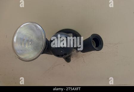 Australian outdoor domestic security motion detector and light fitting with one bulb (globe) removed. About 20 years old. Cobwebs round fitting. Stock Photo