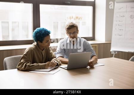 Young multiethnic business colleagues sitting at workplace, looking at laptop Stock Photo